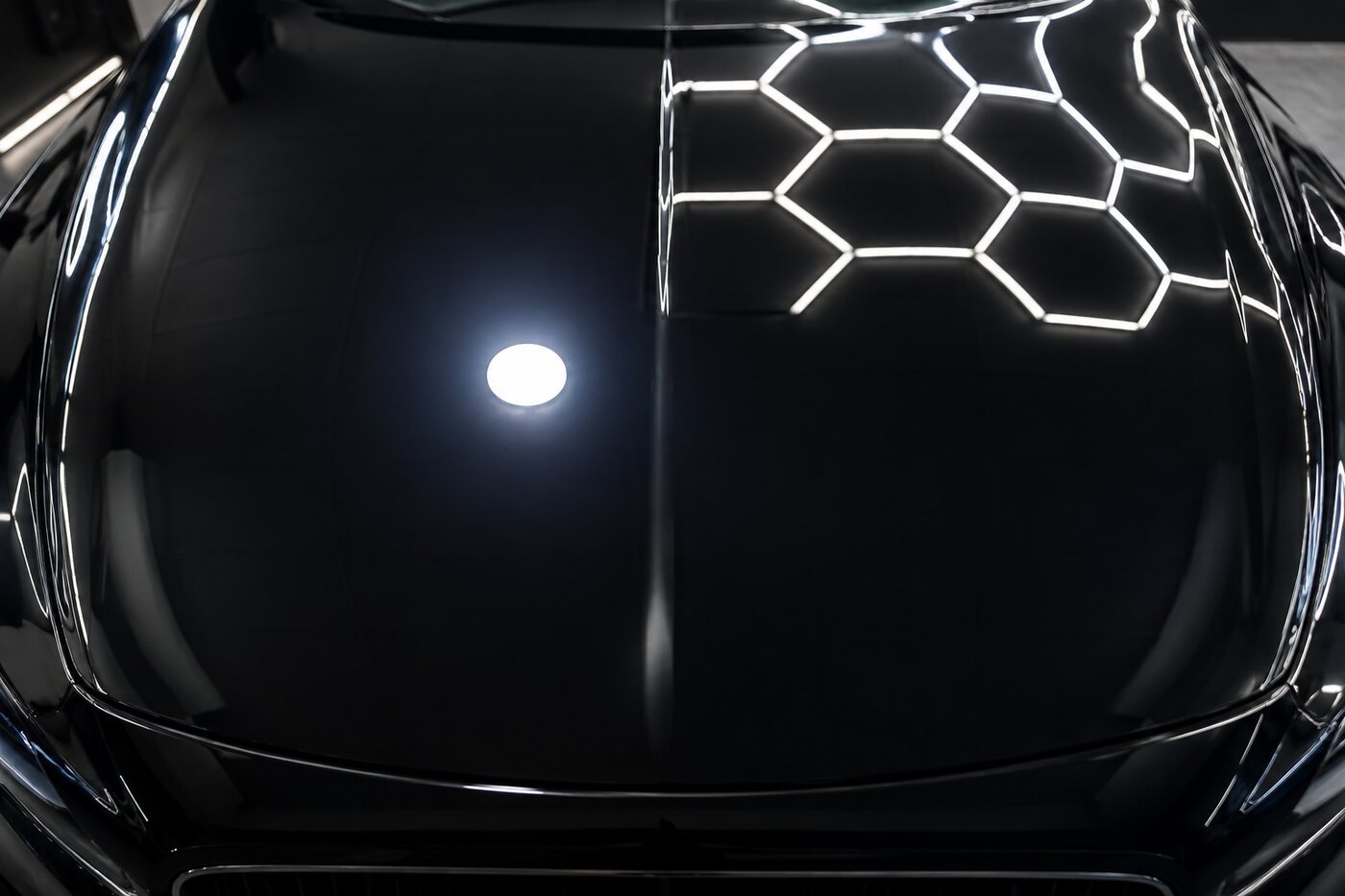 The same black bonnet after paint correction, the inspection light now a clean reflection with no surrounding swirls