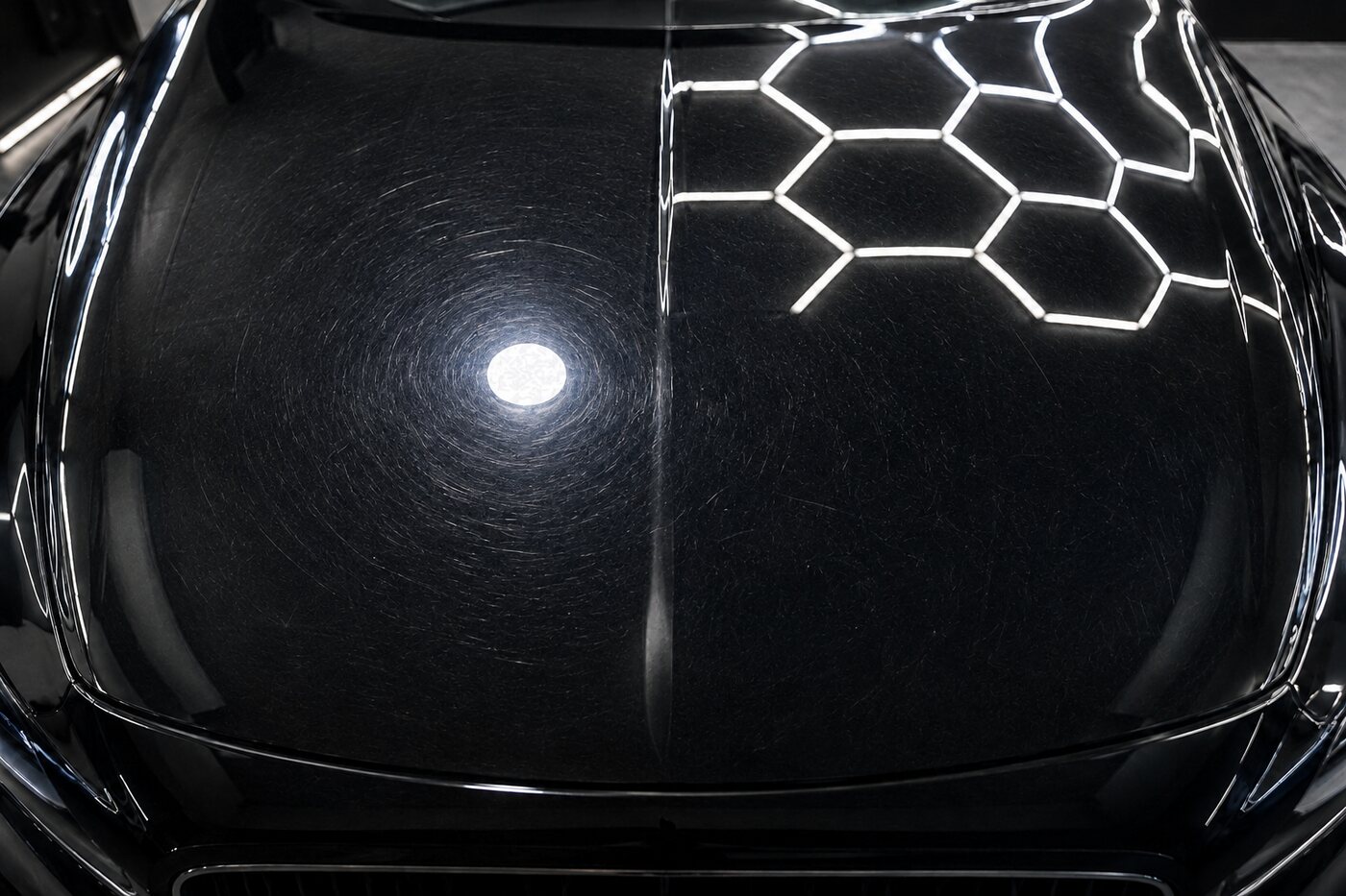 Dense swirl marks and haze circling the inspection light on a black bonnet before paint correction