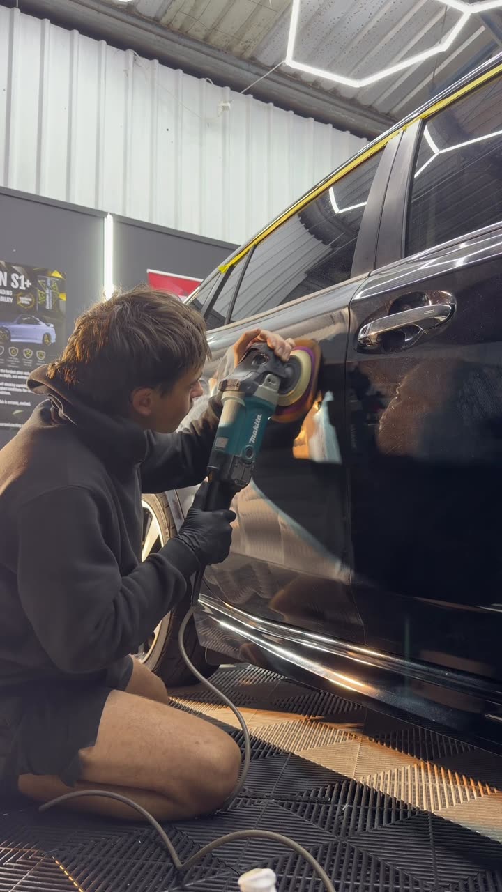 A machine polisher levelling swirl marks out of dark paintwork during a paint correction